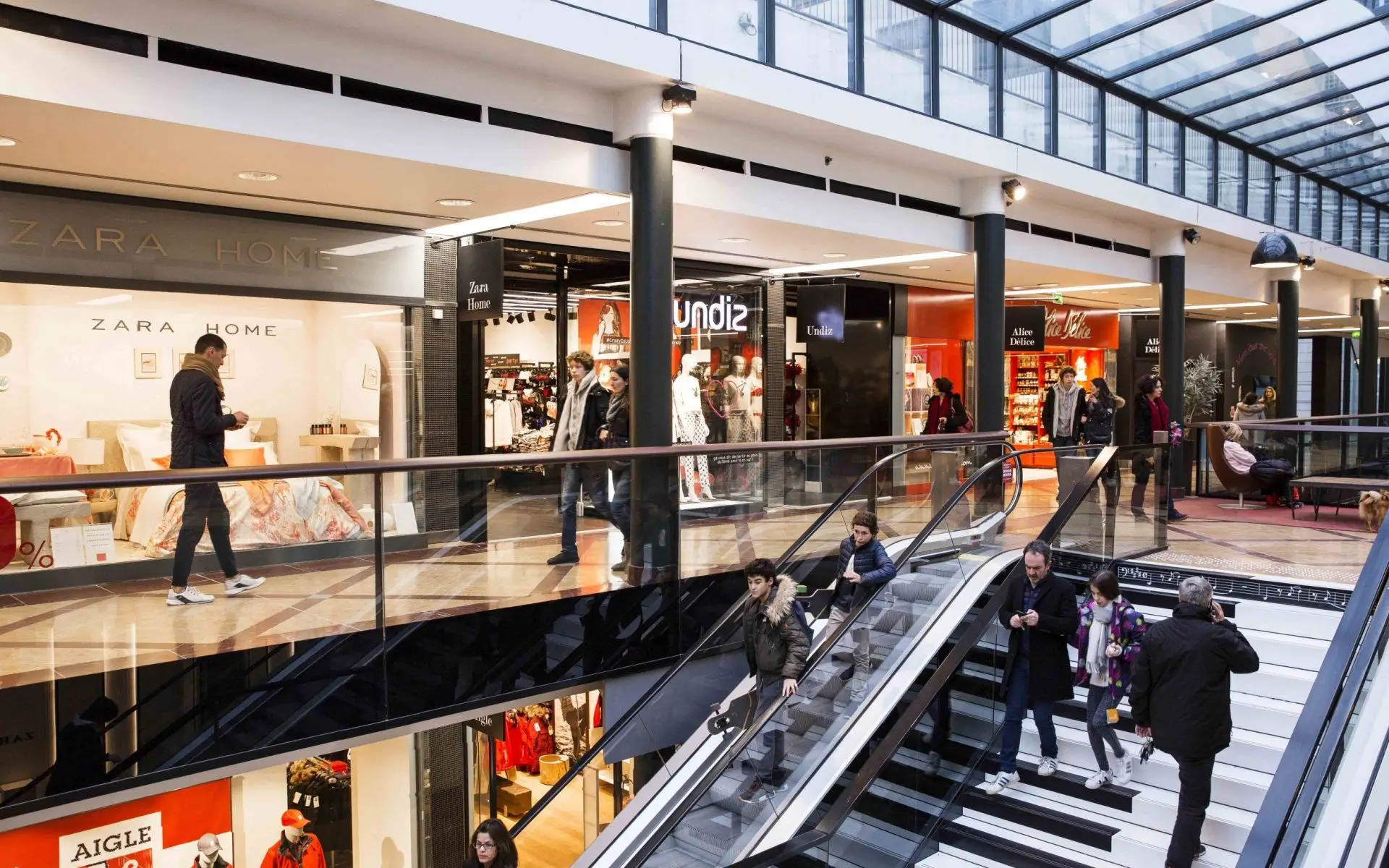 Galerie marchande sur deux niveaux avec escalator, boutiques Zara Home, Undiz et Aigle, visiteurs en circulation